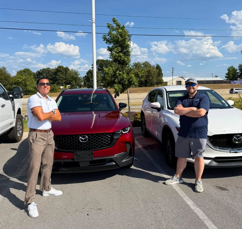 Mario and a client standing by two SUVs on the lot
